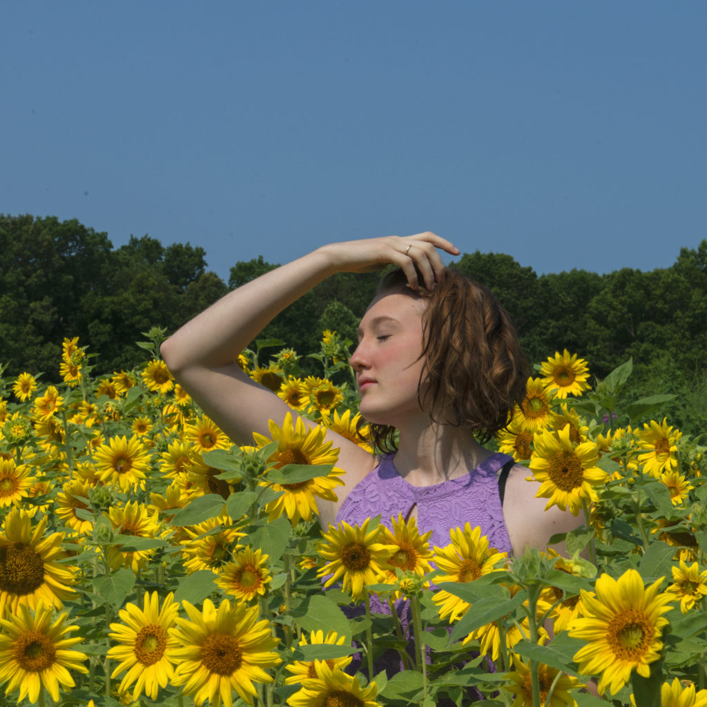 A beautiful young girl brightly photographed in a patch of sun flowers.